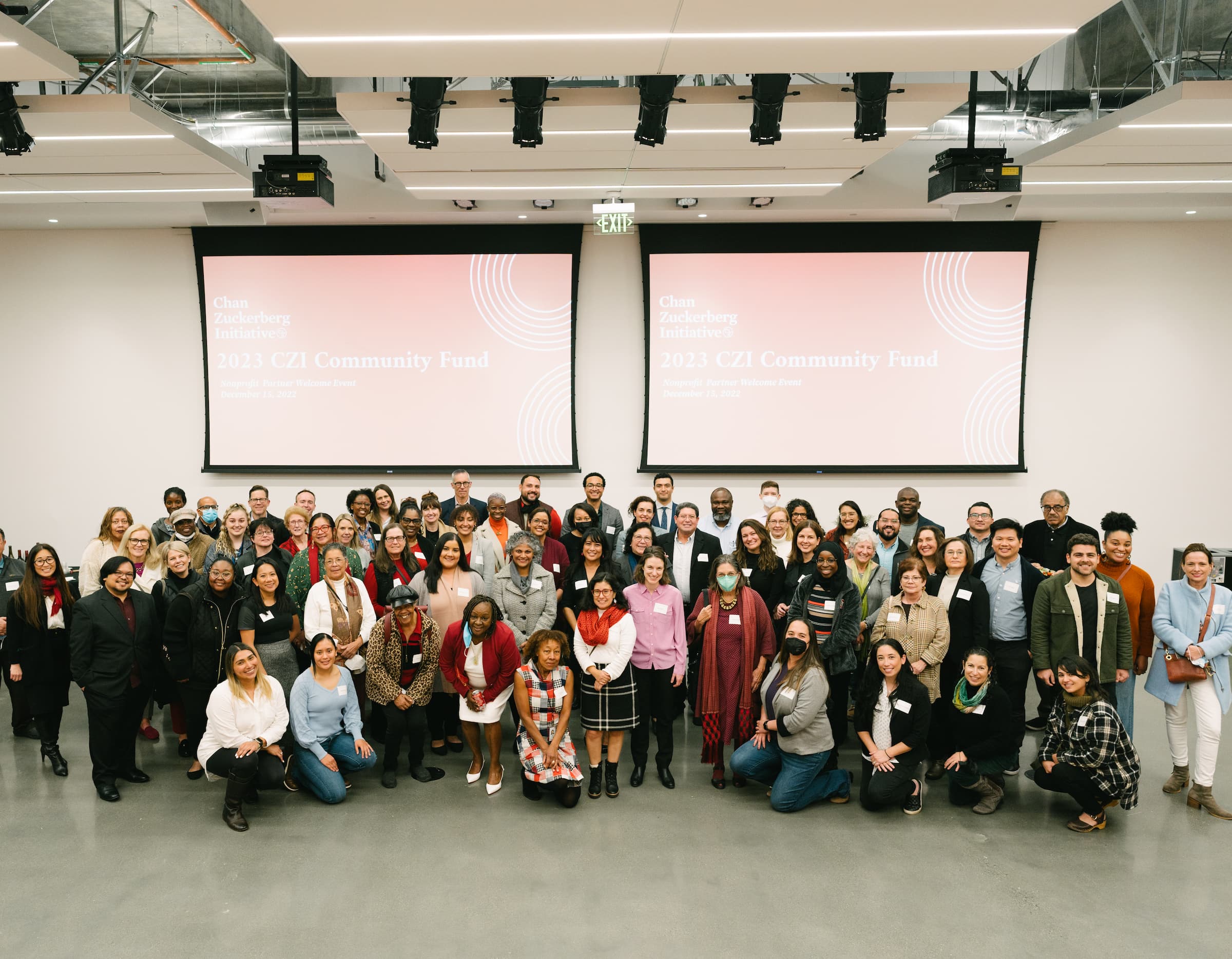 Large group of people poses in front of a wall with two large screens.