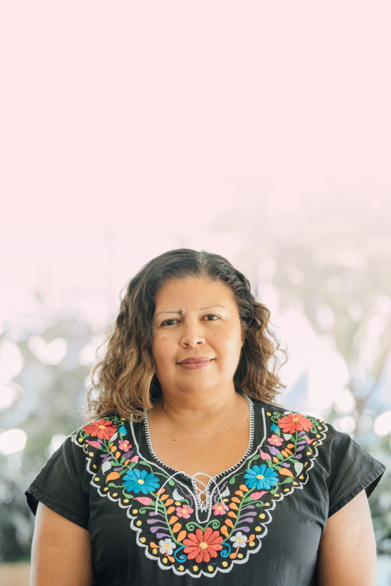 Rosa Cabrera wears a floral-lined blouse and smiles for a headshot while outside.