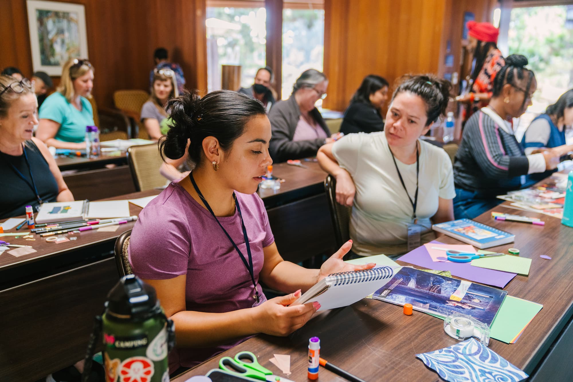 Group of people work with crafting materials while sitting in rows of tables.