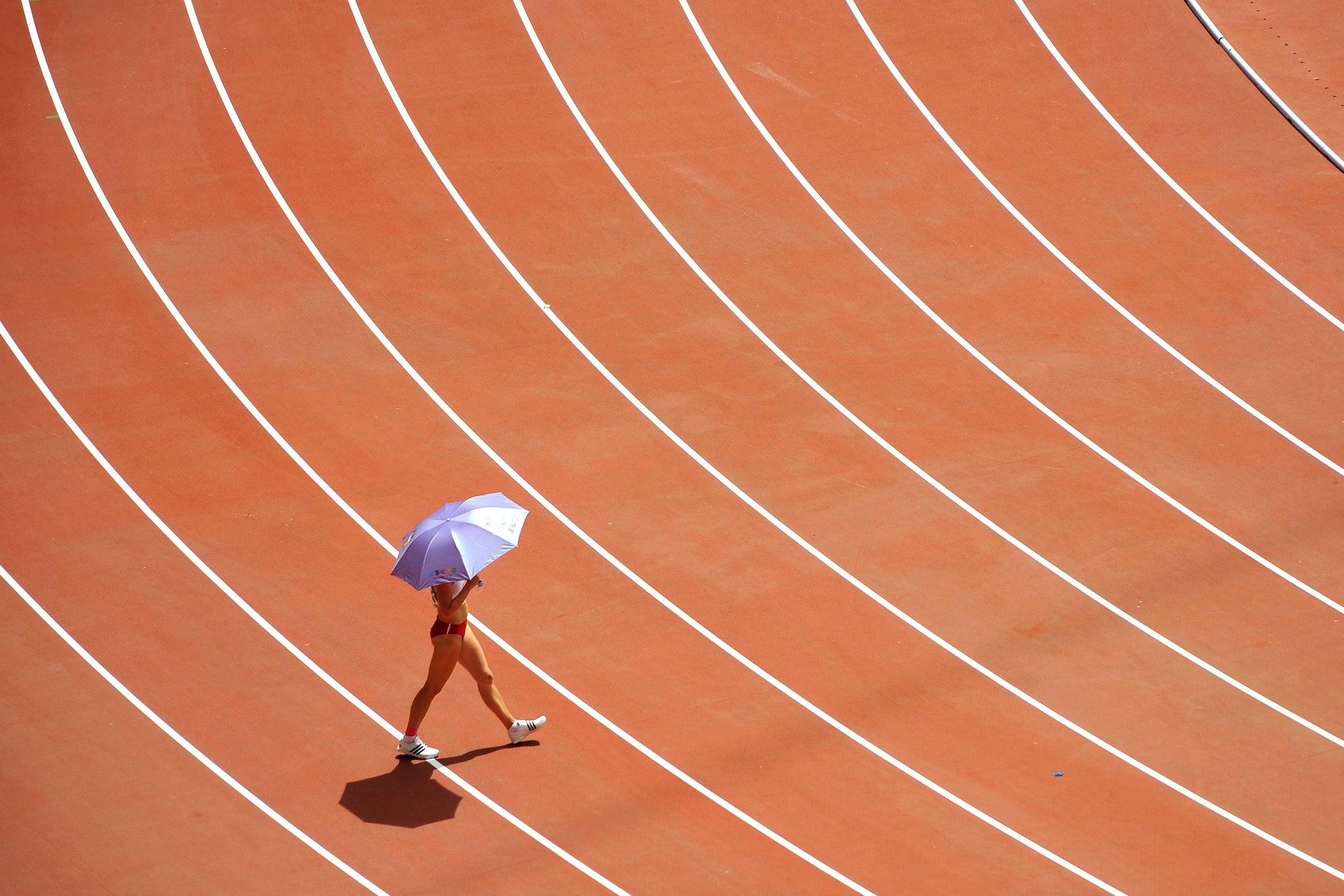 A woman walking across a race track with an umbrella.