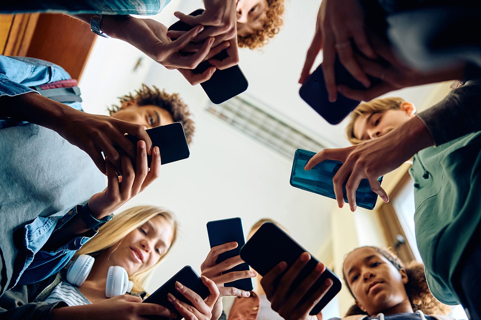 A view from below of a group of teenagers using their smartphones.