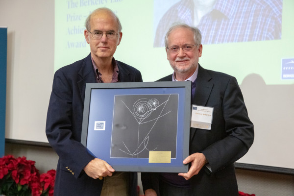 Two people in blue sports coats holding a plaque together, standing side by side.