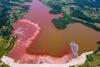 A lake from above with red sludge spreading across its brown waters. There are houses and trees on the banks.