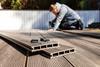 A man uses an electric drill and composite materials to make a decking area in a garden