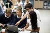 High school students in a science classroom gathered around a laptop