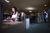 Woman working late at her desk, cleaner vacuuming in background