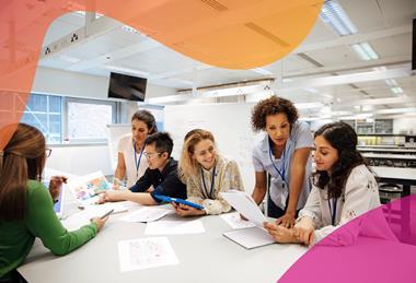 A female teacher works with students in the middle of a large laboratory or classroom, as the students discuss graphs and data printed on paper