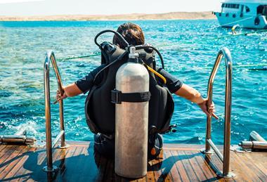 A scuba diver with an air tank sits on the edge of a boat ready to enter the ocean