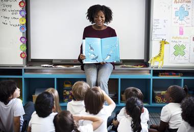 Female primary school teachers reads a book to her class