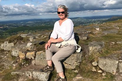 Jill is sitting on some rocks, wearing sunglasses and smiling. There are hills in the background. 