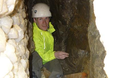 Tom is inside a cave wearing a protective helmet. 