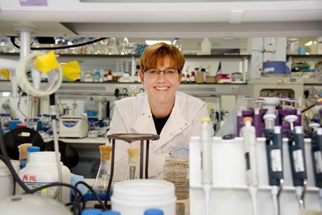 Dr Geertje Van Keulen is smiling in a laboratory filled with equipment and items, including petri dishes and pipettes.