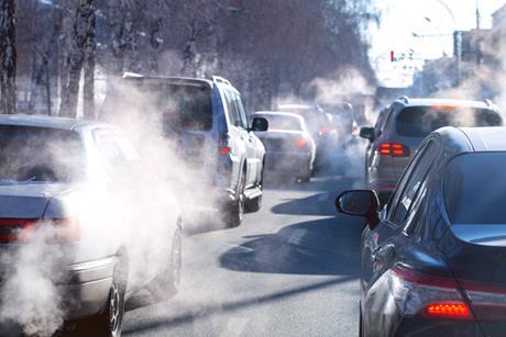 A photograph of queuing urban traffic, showing steam rising from car exhaust pipes