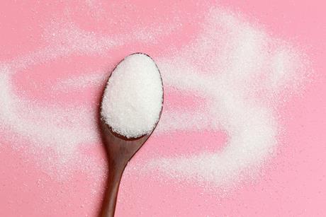 Sugar on a wooden spoon with a pink background