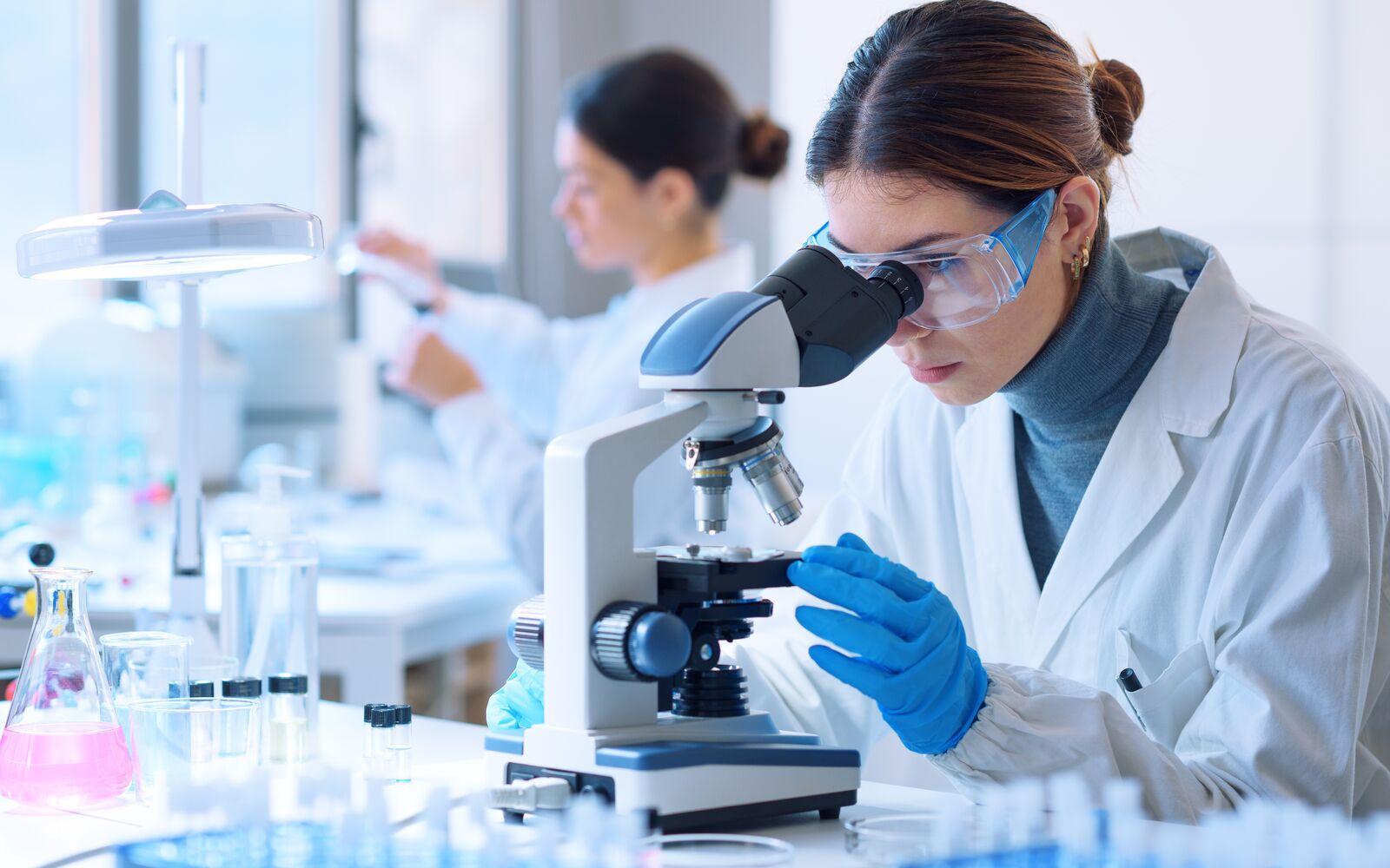 Young scientists conducting research investigations in a medical laboratory, a researcher in the foreground is using a microscope