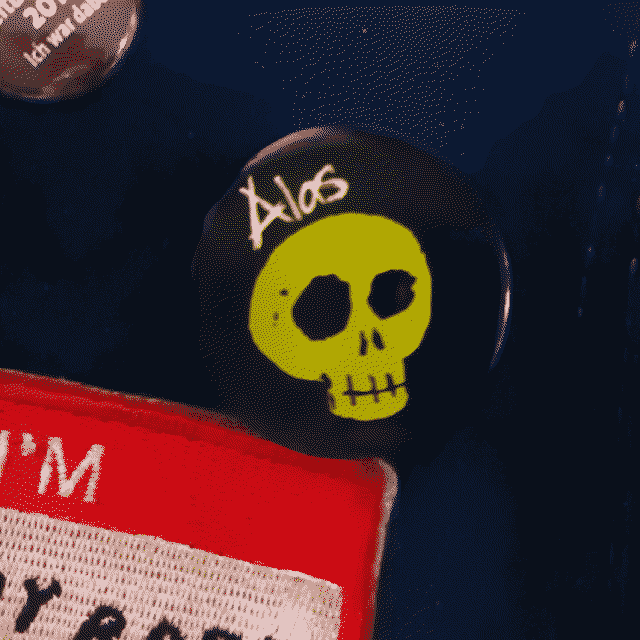 Pin badge. Alas! is the word that stands above a green skull