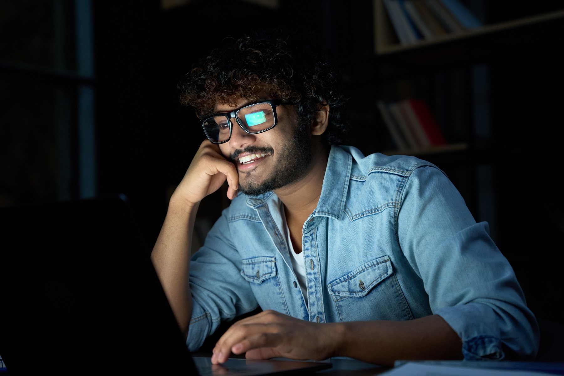 Male student watching laptop in darkened room