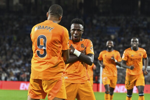 Real Madrid's Kylian Mbappe celebrates with Vinicius Junior, 2nd left, after scoring his side's second goal from a penalty kick during a Spanish La Liga soccer match between Real Sociedad and Real Madrid at the Reale Arena in San Sebastian, Spain, Saturday, Sept. 14, 2024. (AP Photo/Miguel Oses)