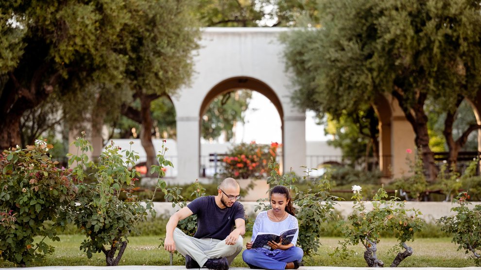 two students sitting, reading a book on campus