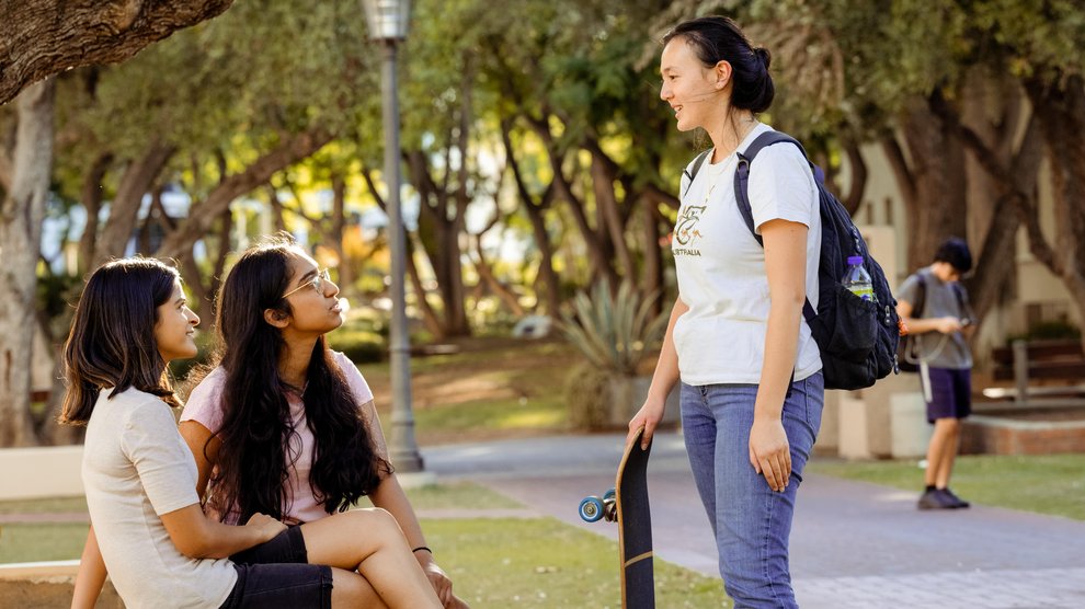 Three students, standing, talking to each other outside of campus