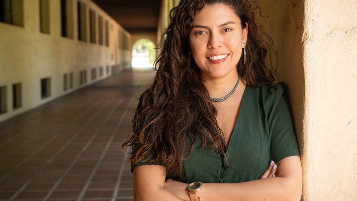 A woman in a green dress stands outside at the Caltech campus for a photo