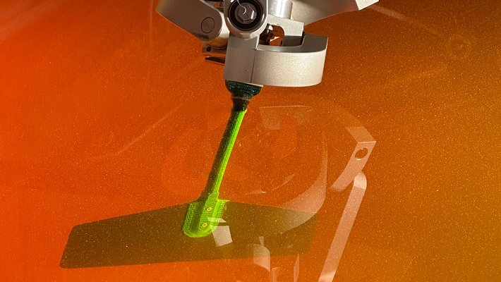 A flapping robot with a green finlike extension is partially submerged in an orange fluid.