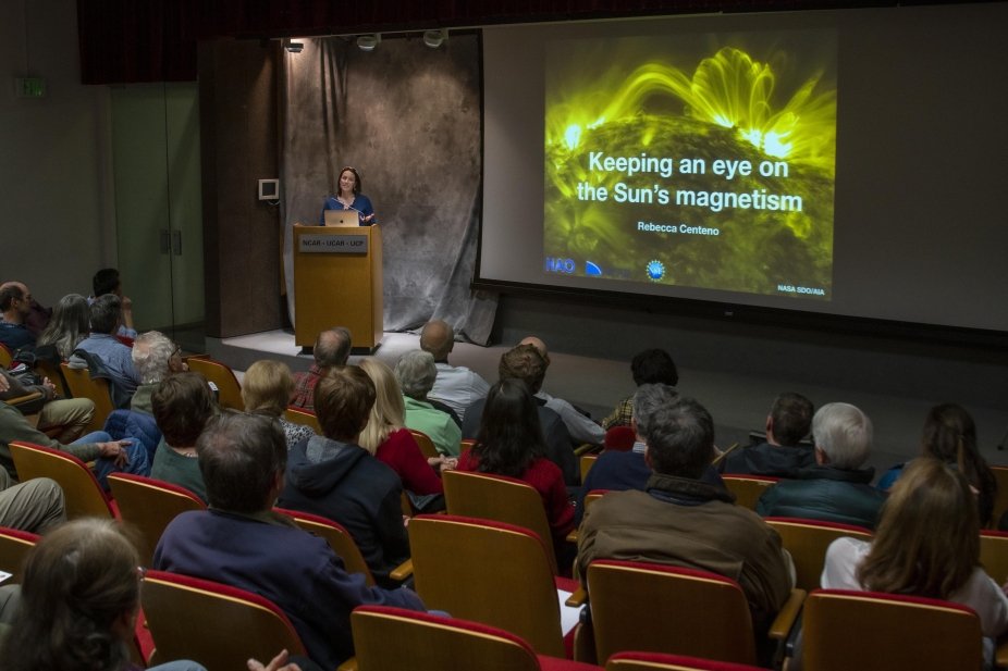 An audience listens to a scientist give a lecture in an auditorium