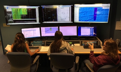 Students map-watching in front of a large display of monitors.