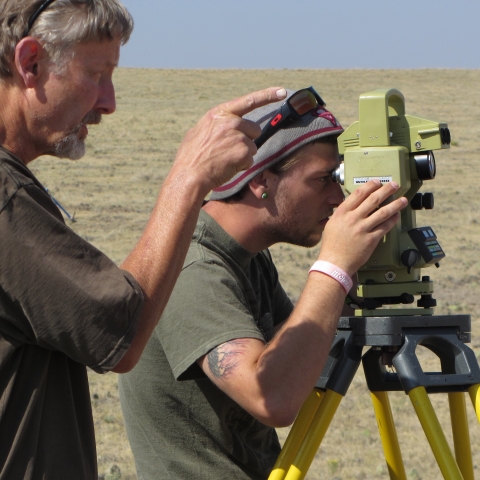 A student looks through an instrument as an instructor points in the same direction. 