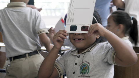 A young student holds 3D glasses up to her eyes.