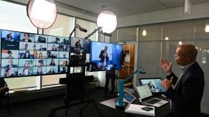 A professor teaches an online course in front of monitors and spotlights.