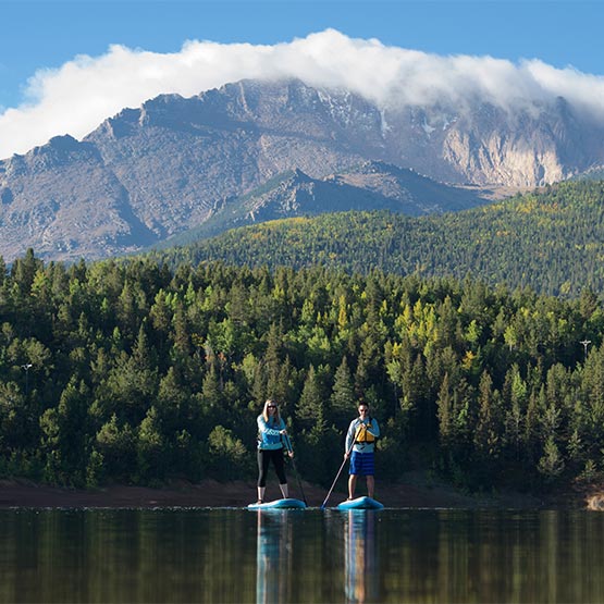 two stand-up paddleboarders on a smooth lake, with the mountains in the background