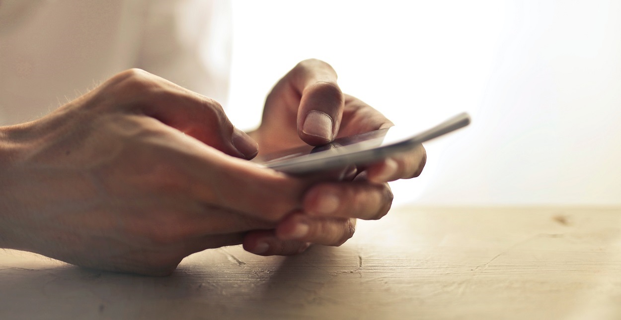 Hands holding a cell phone to call in a report of abuse or neglect.