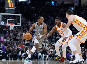 De'Aaron Fox of the Sacramento Kings dribbles the ball while defended by Aaron Holiday and Frank Kaminsky of the Atlanta Hawks