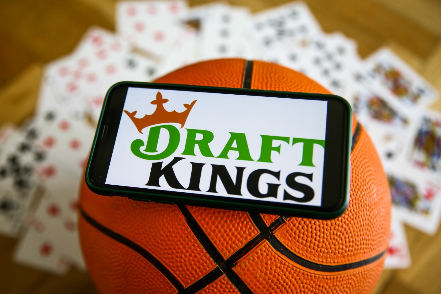 DraftKings logo displayed on a mobile phone, a basketball and playing cards are seen in this illustration photo taken in Krakow, Poland on September 21, 2021. (Photo by Jakub Porzycki/NurPhoto via Getty Images)