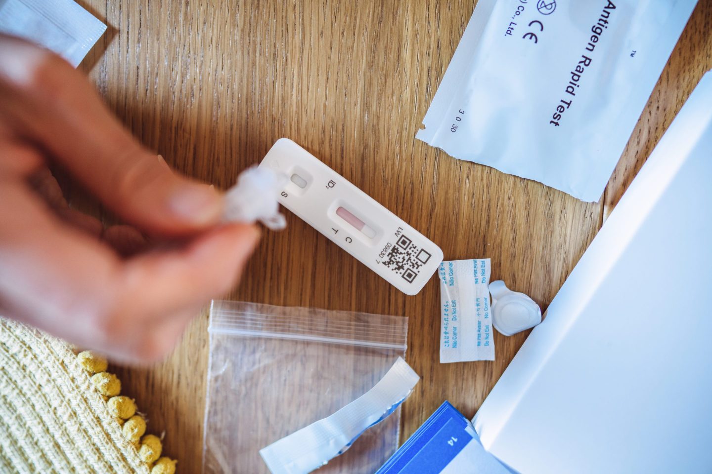 A woman squeezing the sample liquid on a test strip while carrying out a Covid-19 rapid self test at home.