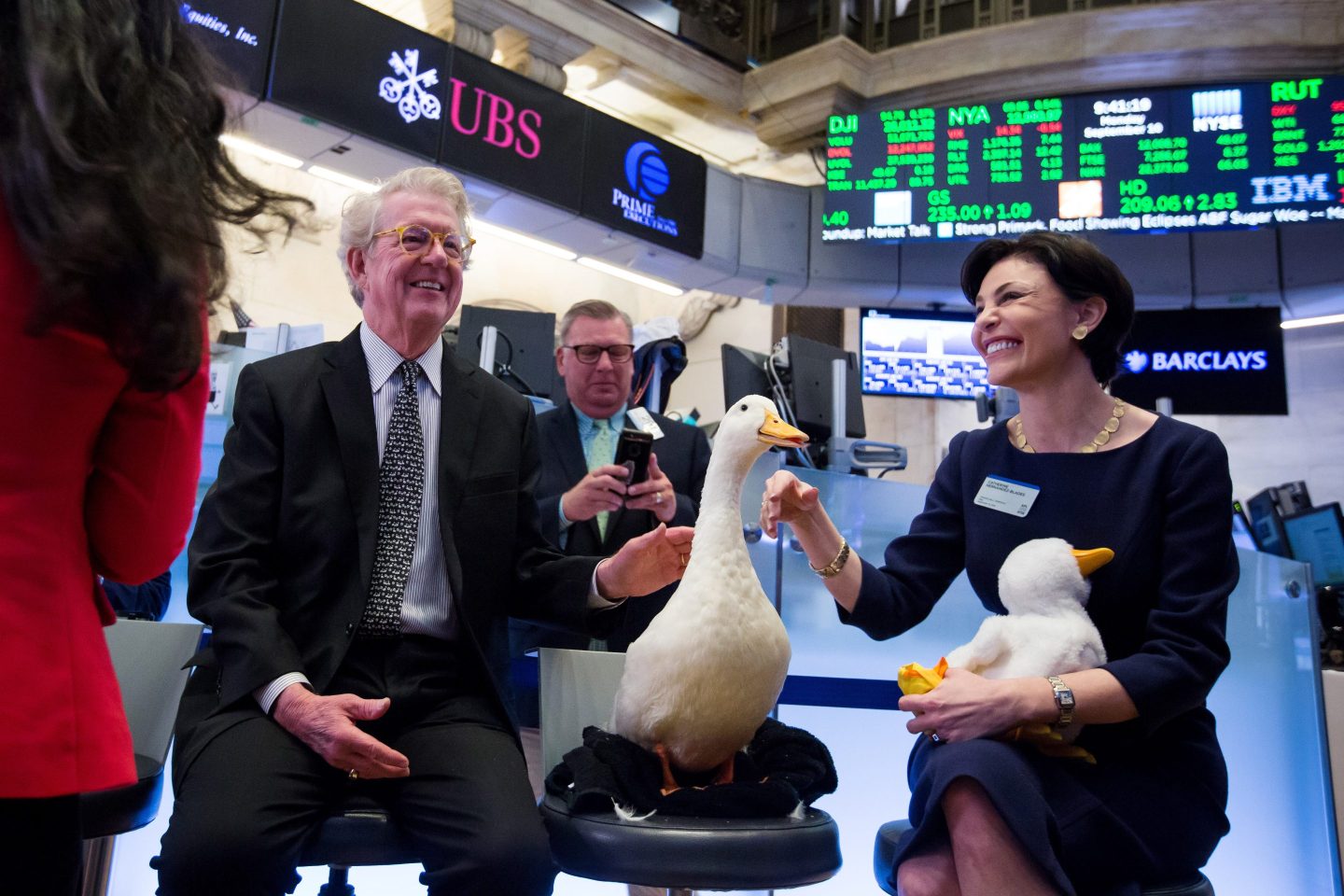 Dan Amos, chairman and chief executive officer of Aflac Inc., left, and Catherine Hernandez-Blades, chief brand and communications officer of Aflac Inc., right, pet the Aflac duck on the floor of the New York Stock Exchange (NYSE) in New York, U.S., on Monday, Sept. 10, 2018. Stocks held early gains even as shares of Apple and Asia-based suppliers slumped after President Donald Trump insisted his trade war with China will spur more manufacturing jobs in the U.S. Photographer: Michael Nagle/Bloomberg via Getty Images