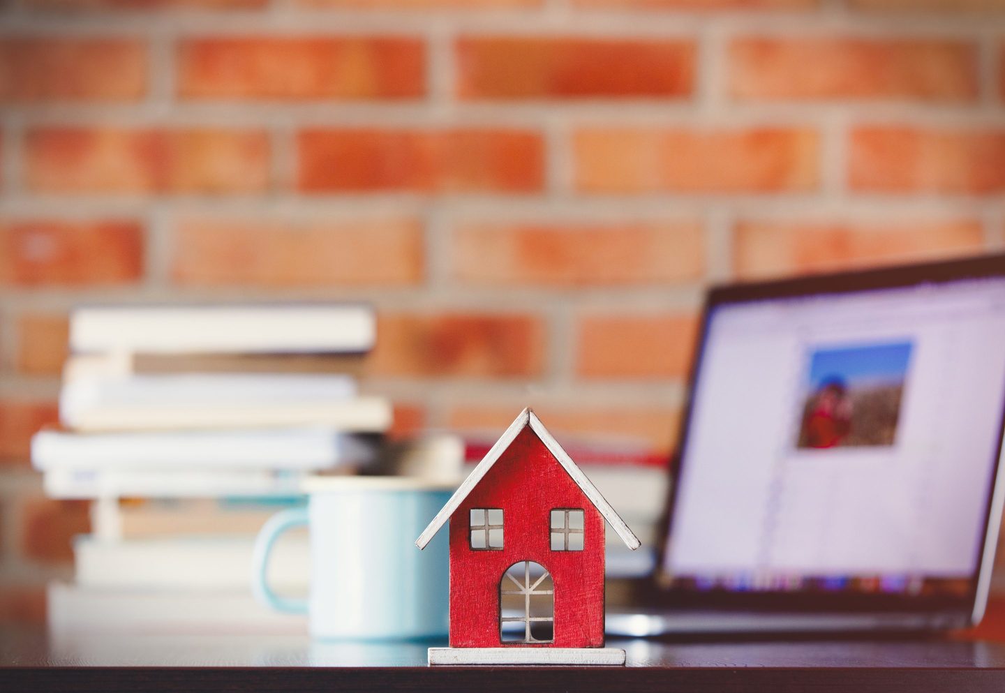 Small house toy on a table in front of a laptop, books, and coffee mug.