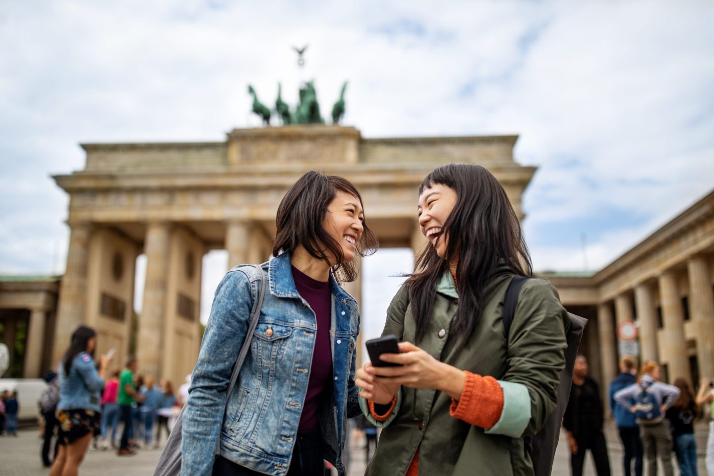 Cheerful female friends standing against Brandenburg Gate during vacation.