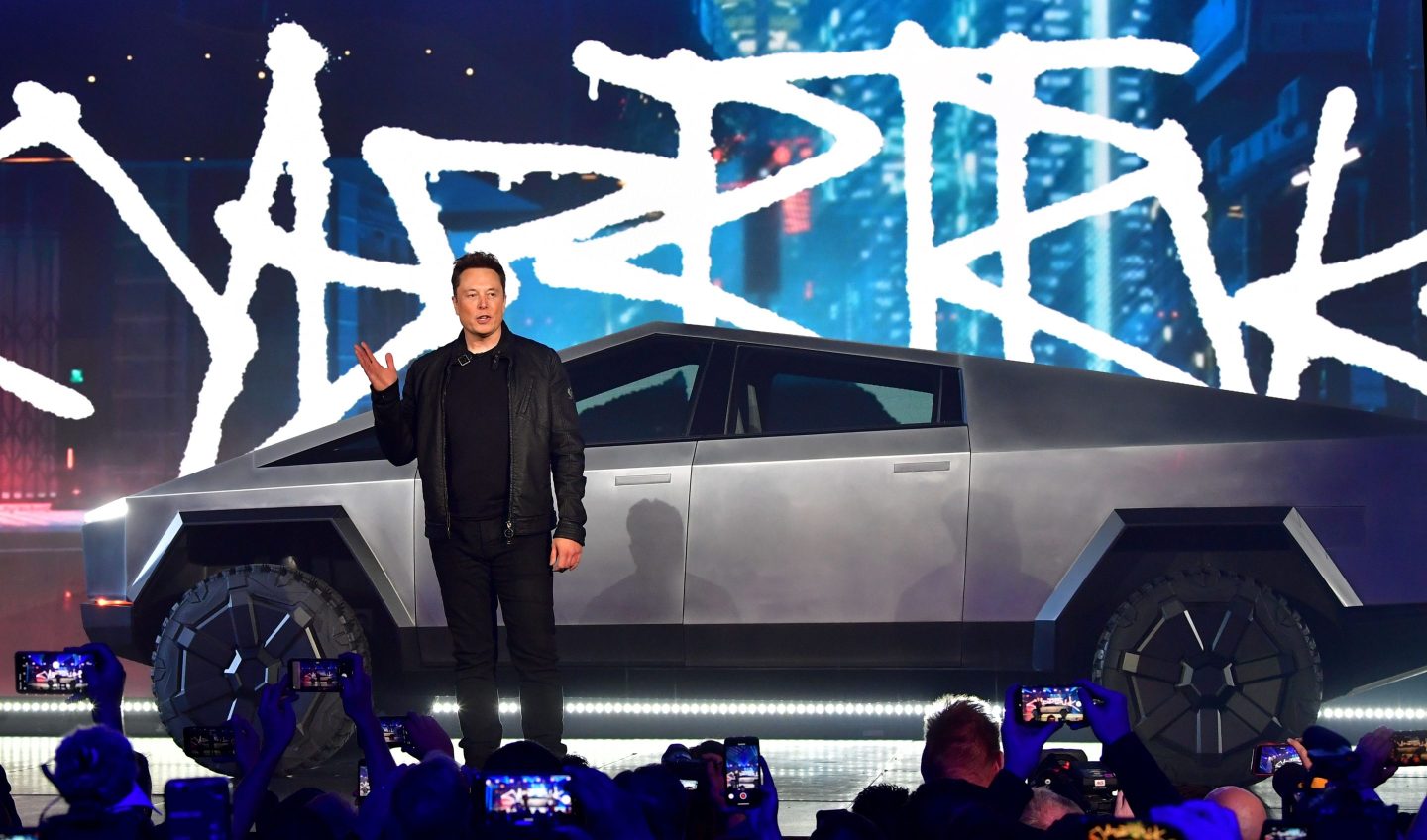 Elon Musk stands in front of a Cybertruck at a presentation.