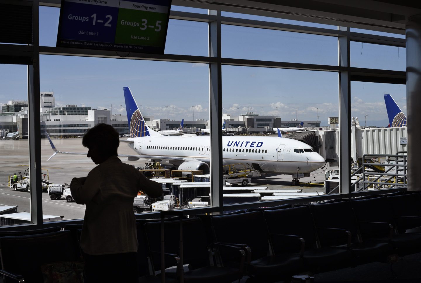 Passenger waiting for her flight to board stands in the airport terminal as a United Airlines plane is loaded at a gate at Airport