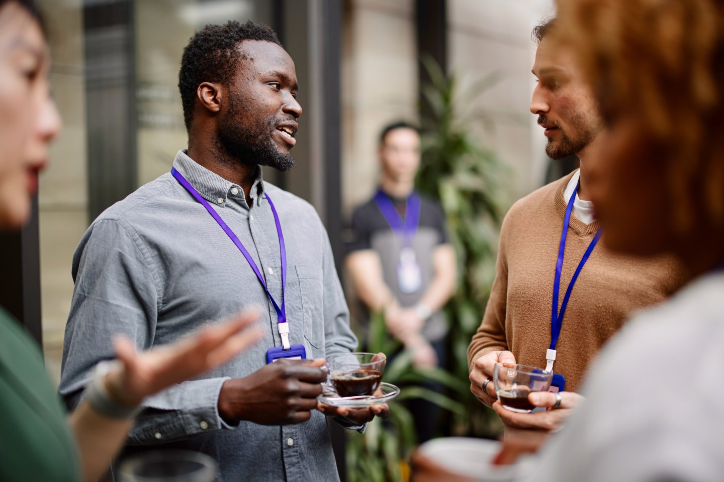 Entrepreneurs drinking black coffee while standing with colleagues in convention center.