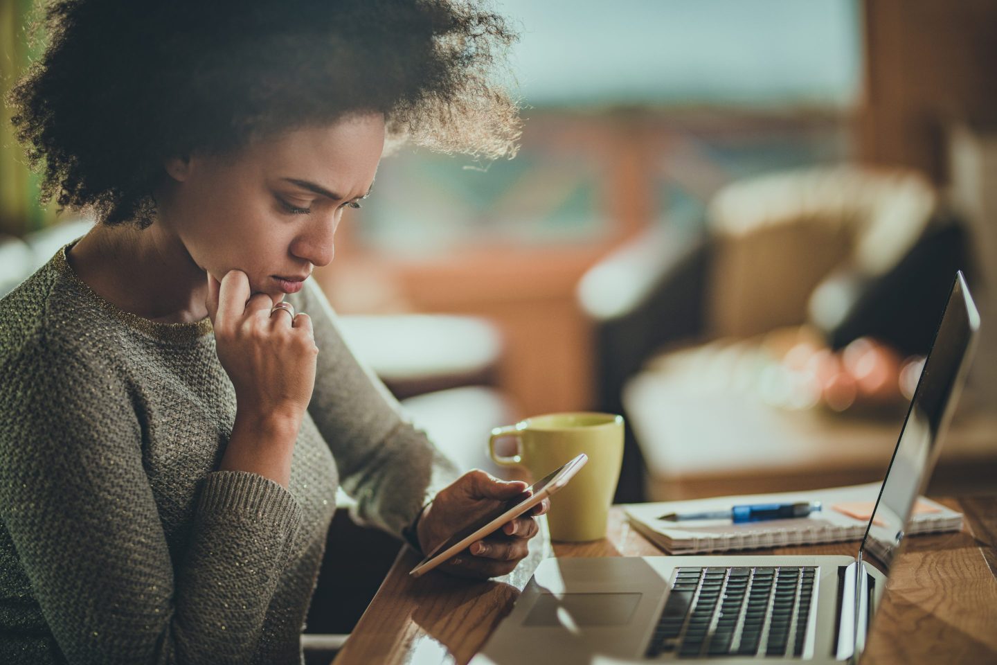 Woman looking anxiously at her phone while sitting in front of her laptop