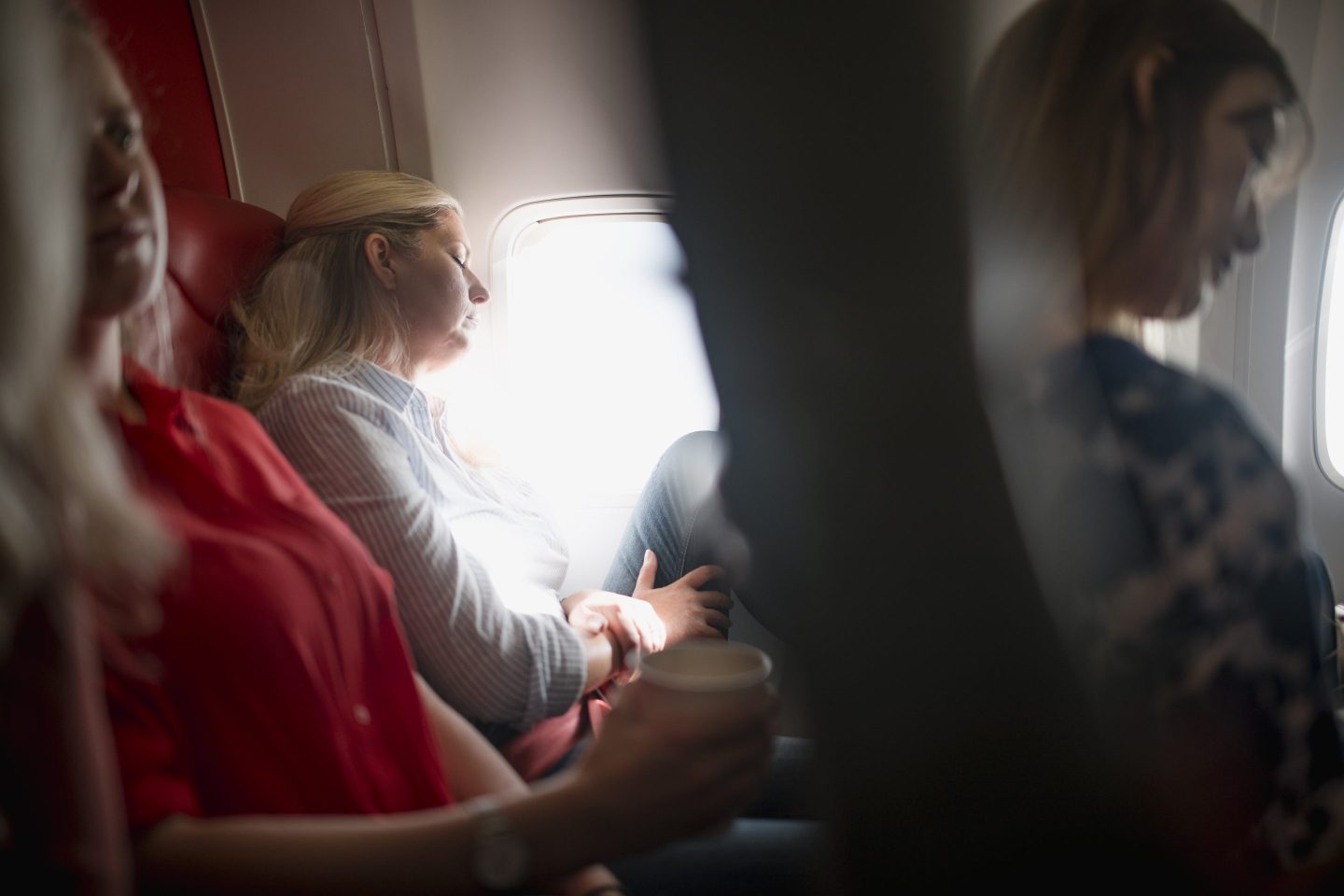 Woman sleeps surrounded by other women on plane.