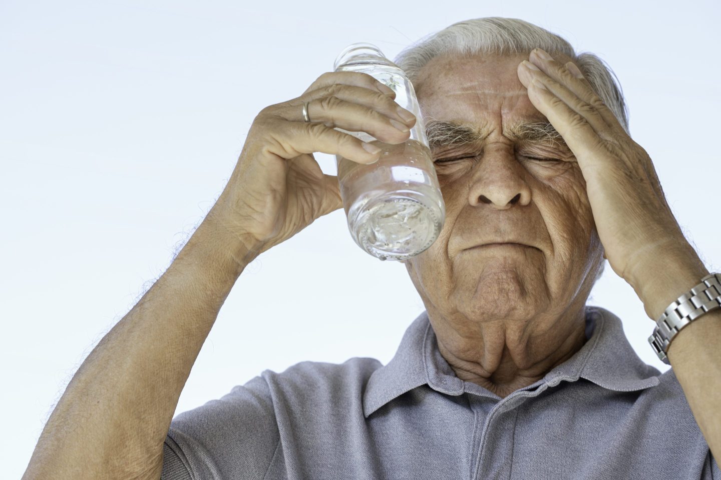 Senior man is trying to cool himself using a water bottle touching his head.  Representing heat wave solutions.