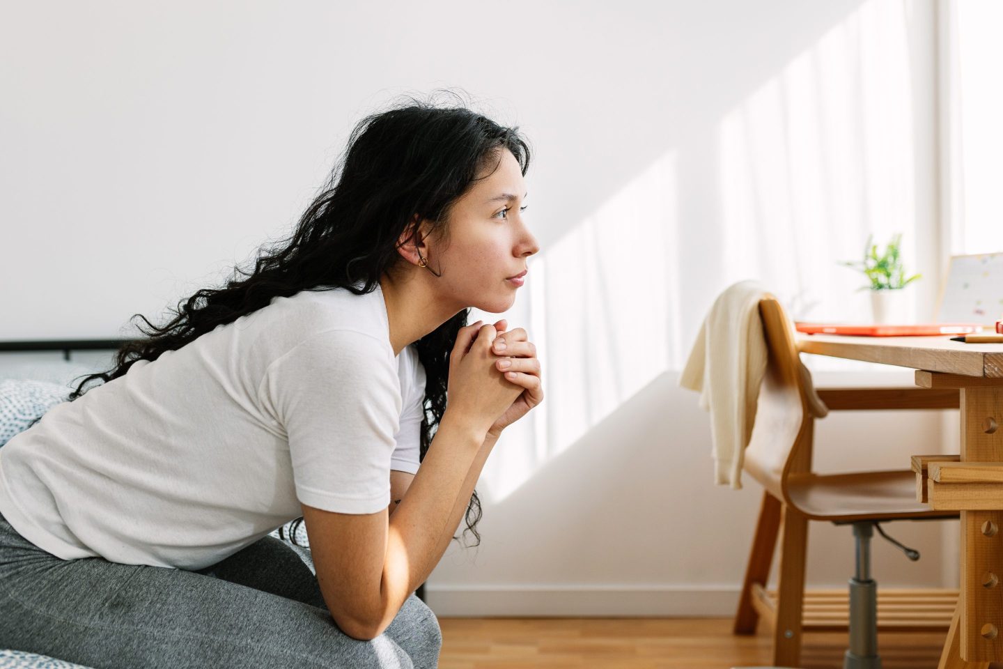 Sad and lonely thoughtful teenage girl looking away sitting on bed in the room. Social issue and adolescence bullying concept