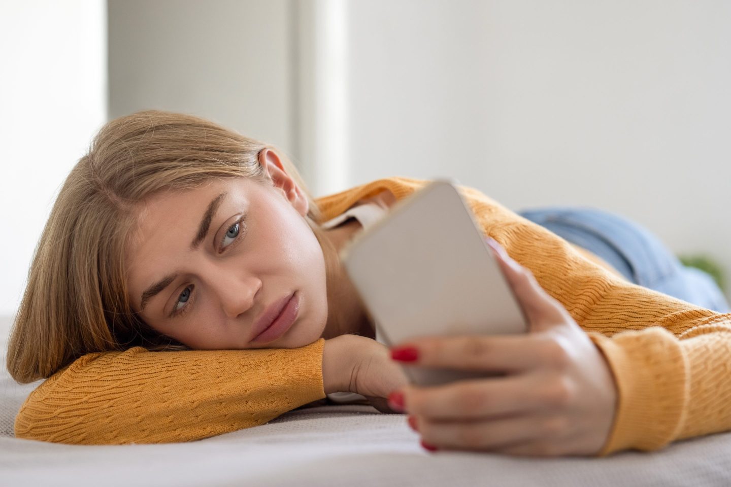 Woman lying on bed while scrolling through social media on phone