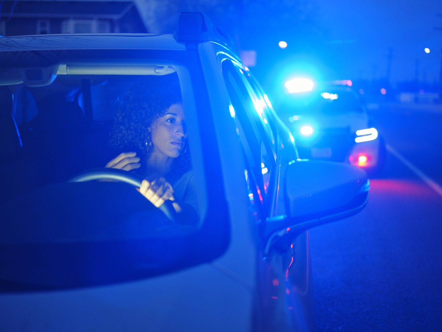 young woman at the wheel of a car at night, police lights in the background