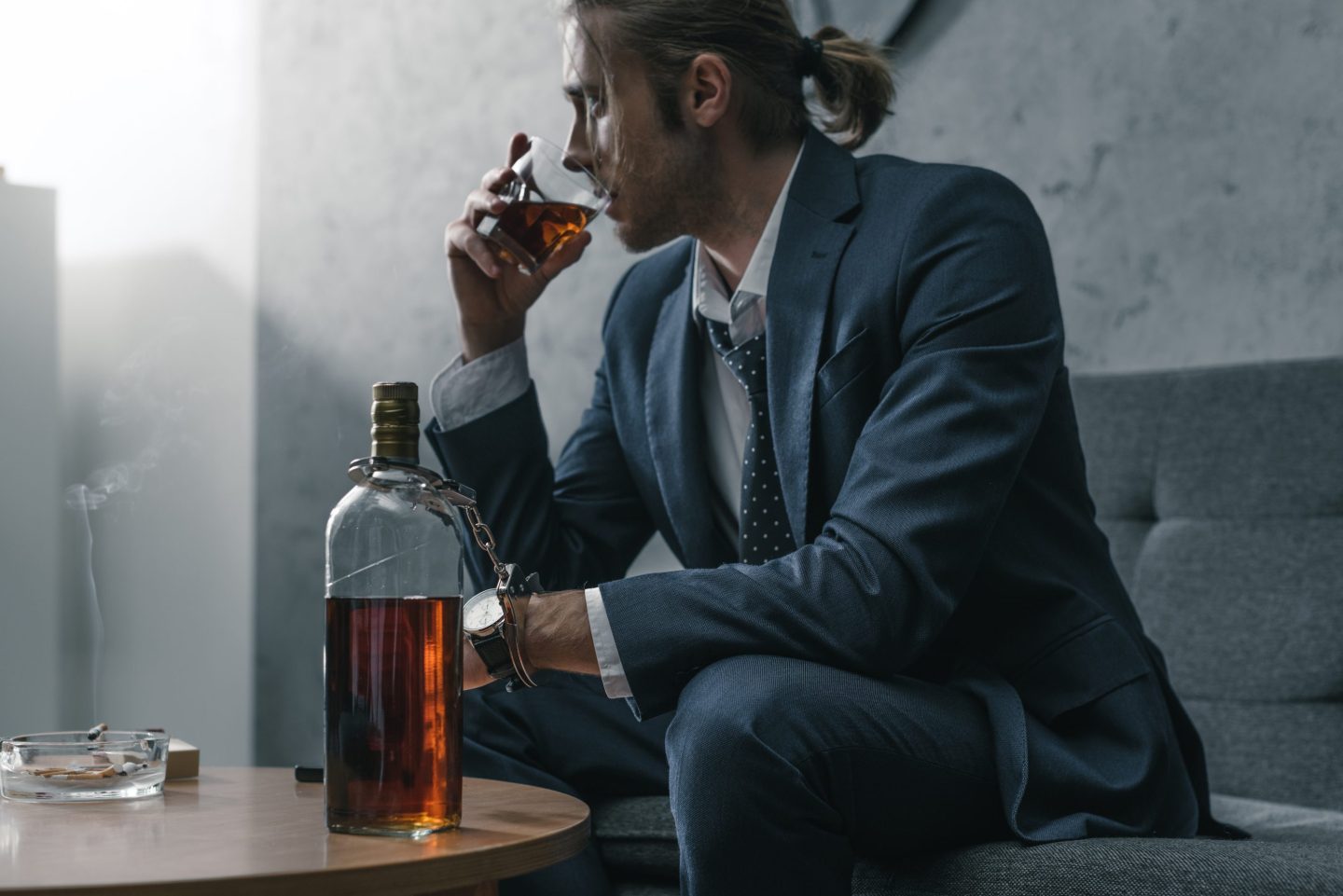 A young man in a business suit drinks whiskey on a sofa