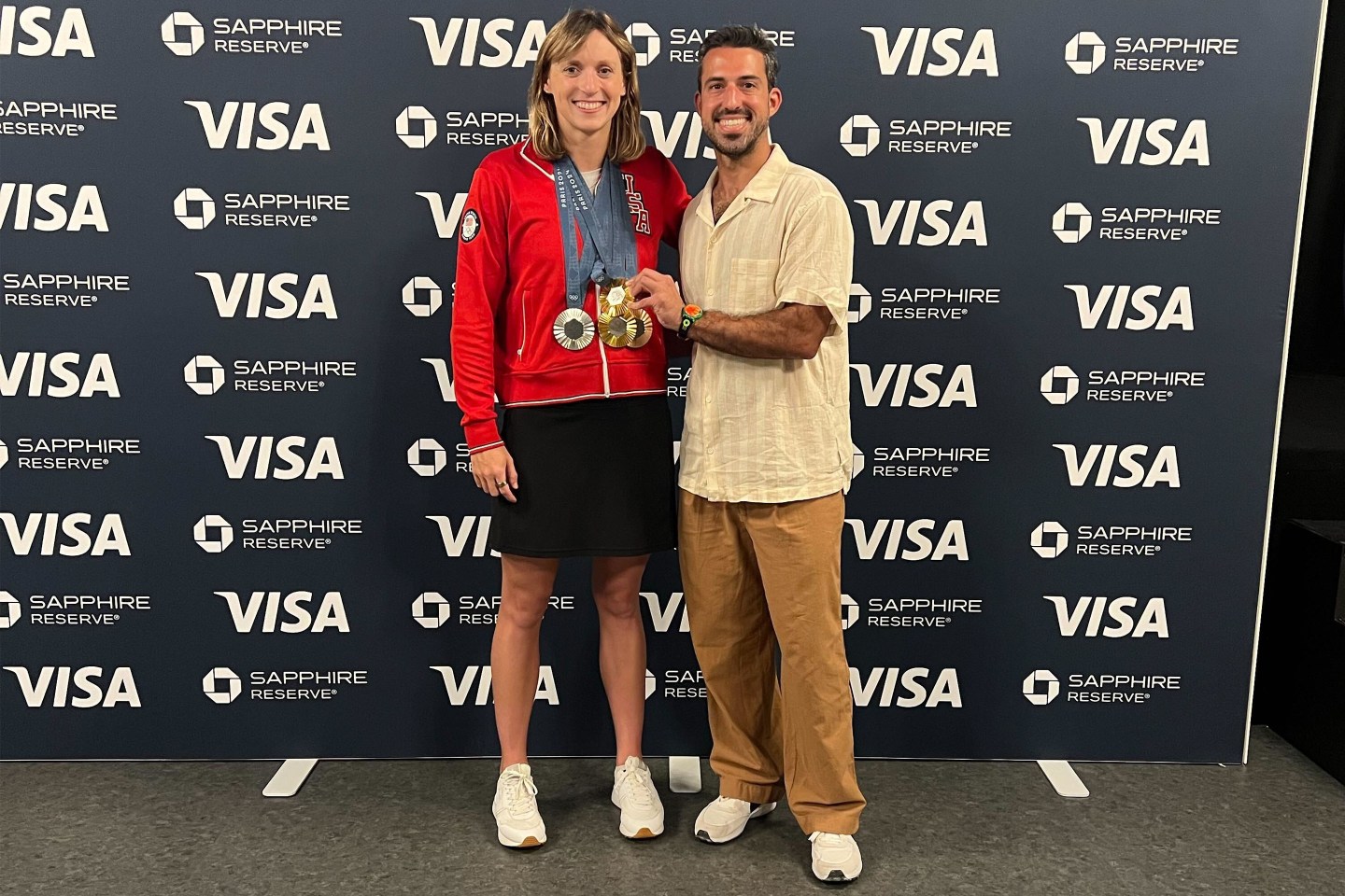 Andrew Schwartz standing next to Katie Ledecky and her gold medals in the Chase Sapphire Lounge at the Paris 2024 Olympics.